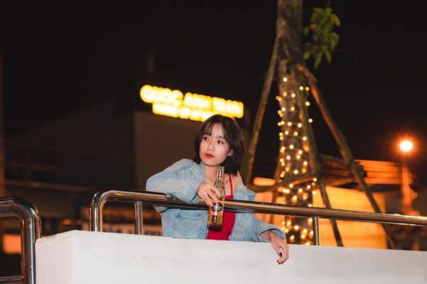 woman-standing-by-the-railing-while-holding-a-bottle-3653029